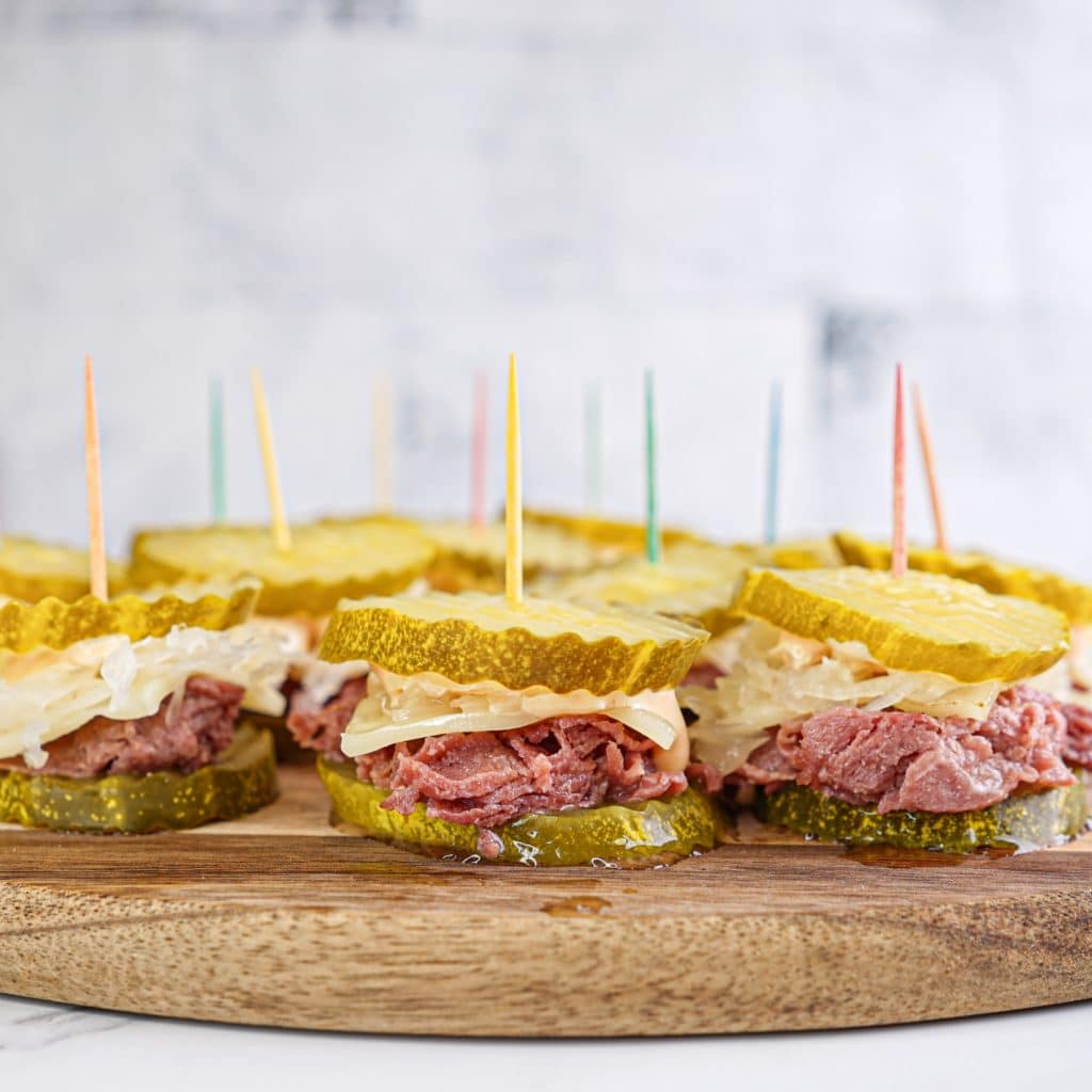 Close up recipe photo showing pickle slices with corned beef, sauerkraut, and cheese between.