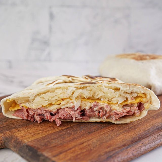 Reuben ingredients layered in a Crunchwrap tortilla on a board