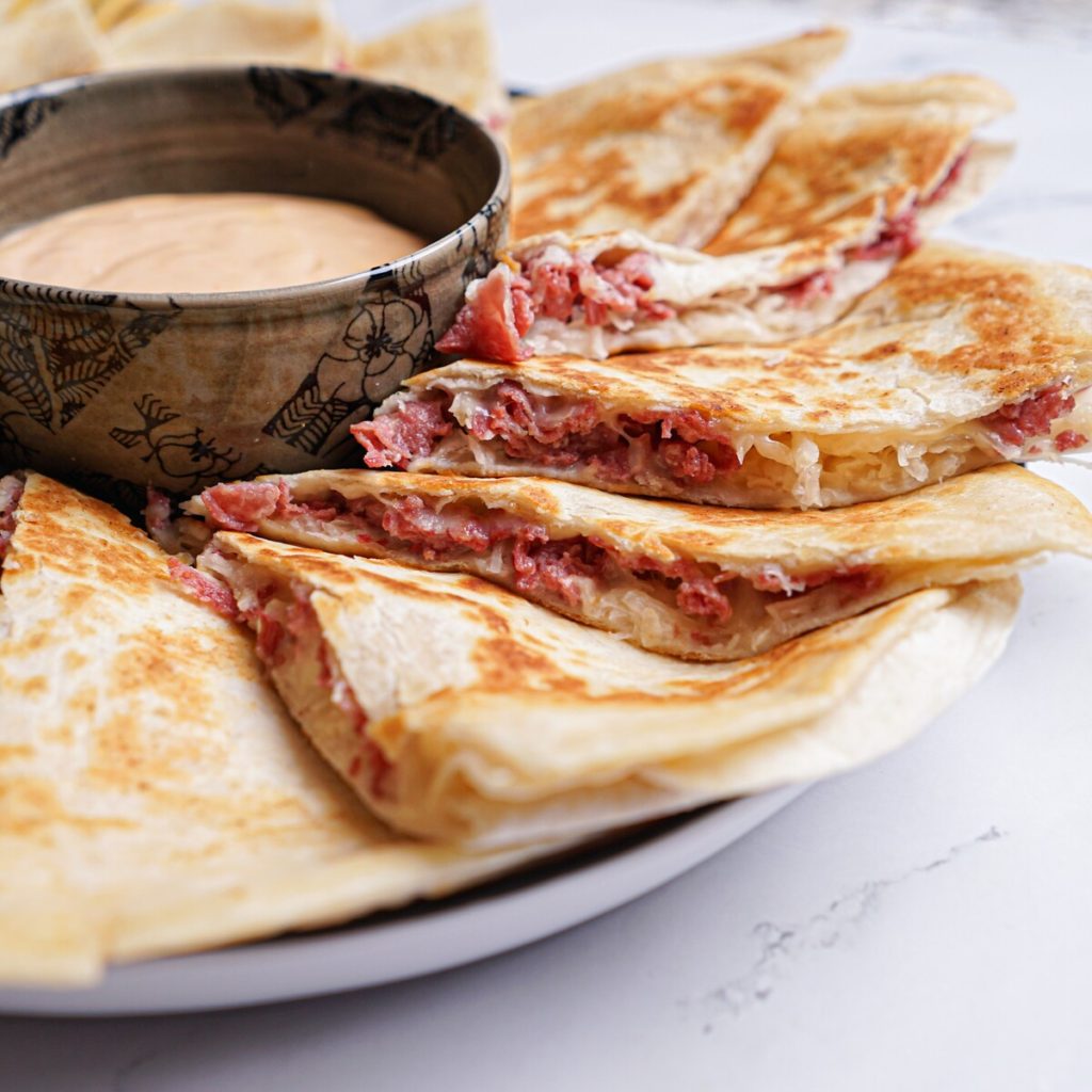 Slices of quesadilla open to see Reuben filling on a plate