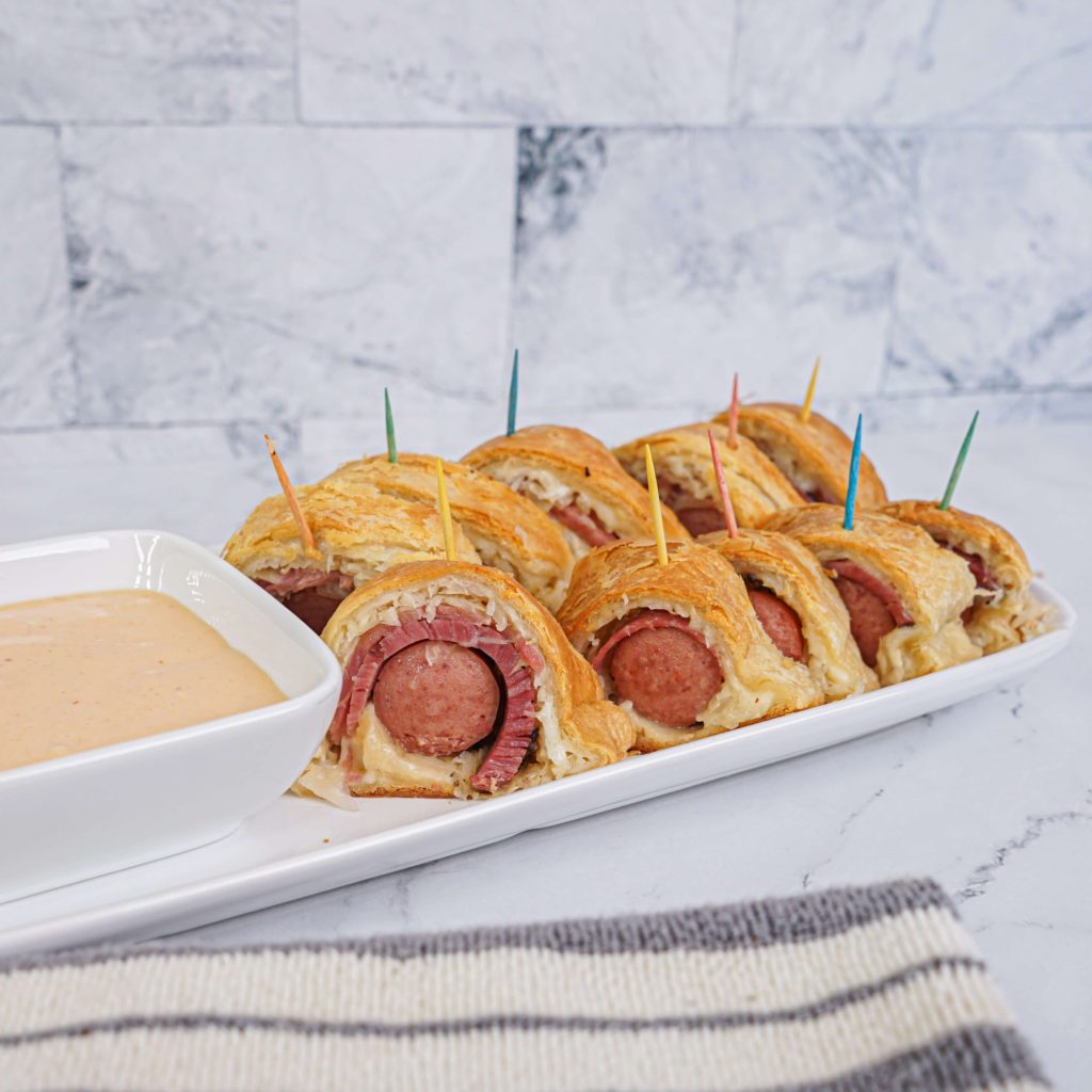 Reuben pigs in a blanket on a white plate with dipping sauce