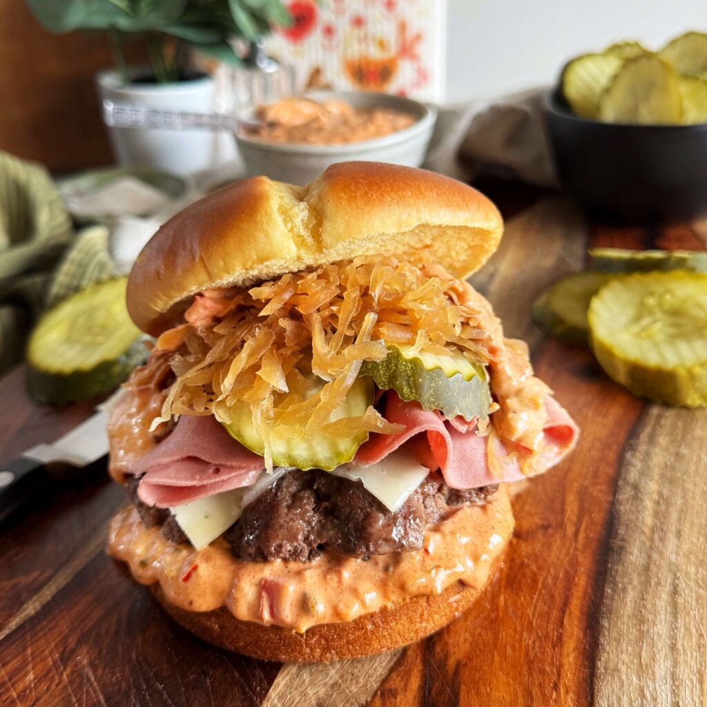 Reuben Burgers with BBQ Kraut, Dill Pickles, and Zesty Thousand Island Dressing on a wooden cutting board