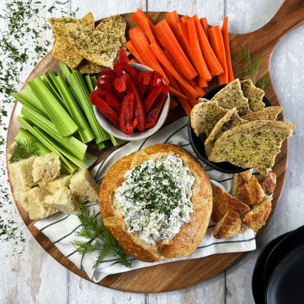 Kraut and Dill Pickle Dip in a Bread Bowl on a wooden tray.