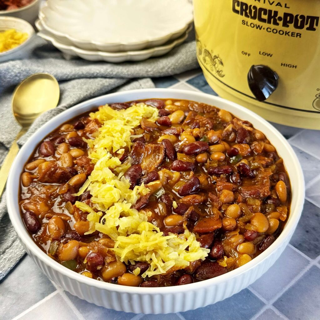 A bowl of Slow Cooker BBW Baked Beans with Frank's Mustard Kraut. With a Vintage Crock pot in the background.