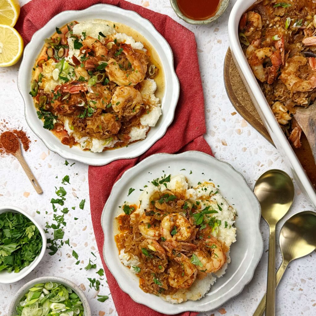 Two white round plates with Baked Cajun Shrimp with BBQ kraut on top of either grits or rice.