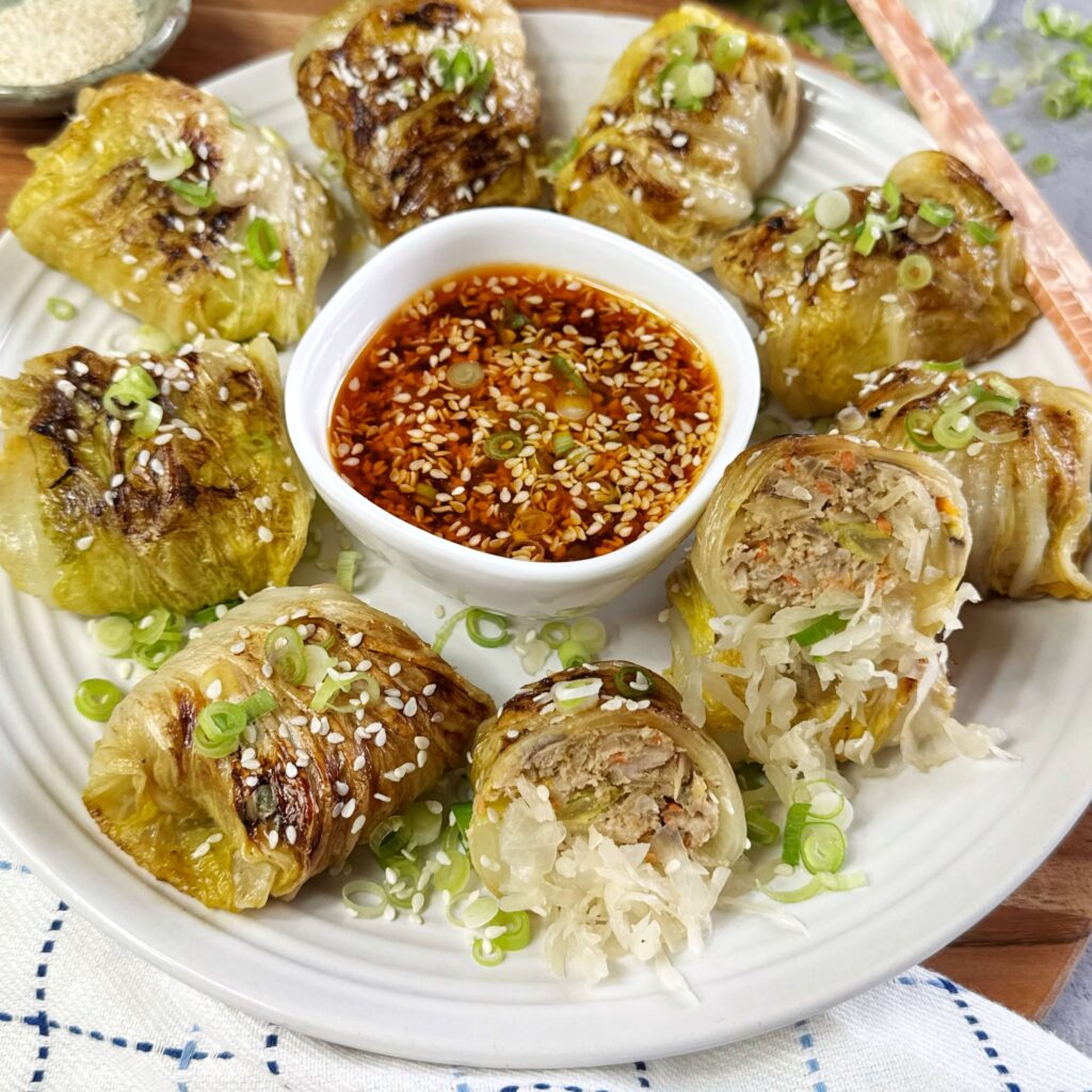 Kraut and Pork Stuffed Cabbage Dumplings with Dumpling Sauce on a white dinner plate.