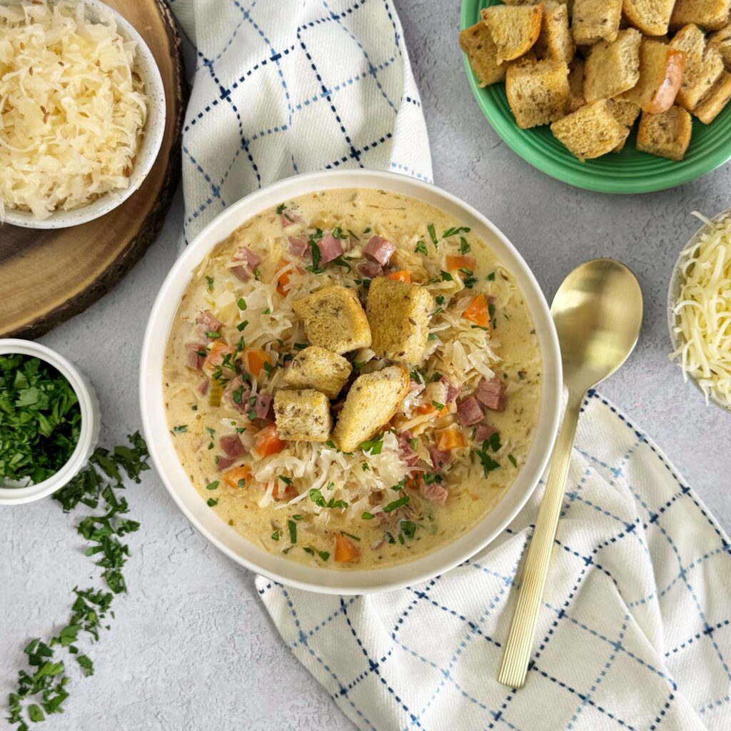 A warm bowl of Creamy Reuben Soup with Bavarian Kraut and Rye Croutons in a white soup bowl.