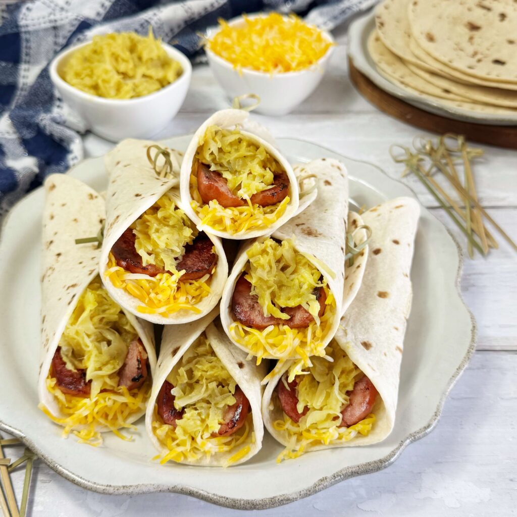 A white dinner plate with Sausage and Mustard Kraut Roll up's stacked on a plate.