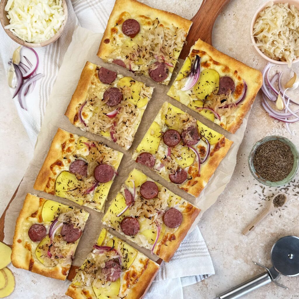Homemade potato, kraut, and smoked sausage pizza topped with melted cheese and Frank's Kraut, sliced and ready to serve.